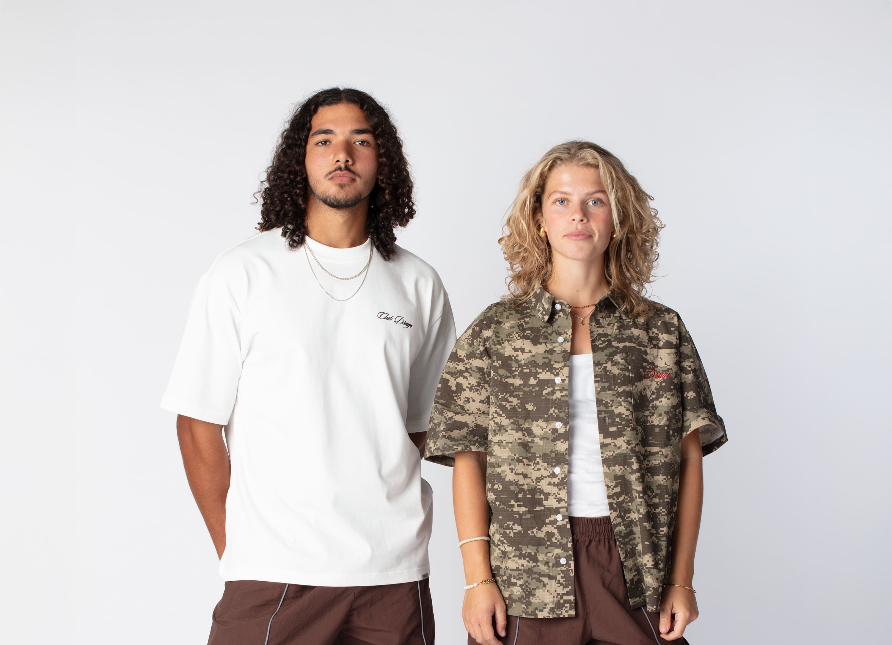 Ahmed wearing our oversized sun t-shirt and brown track pants, and Nikoline wearing our Short sleeve shirt in camo and our track pants cacao
