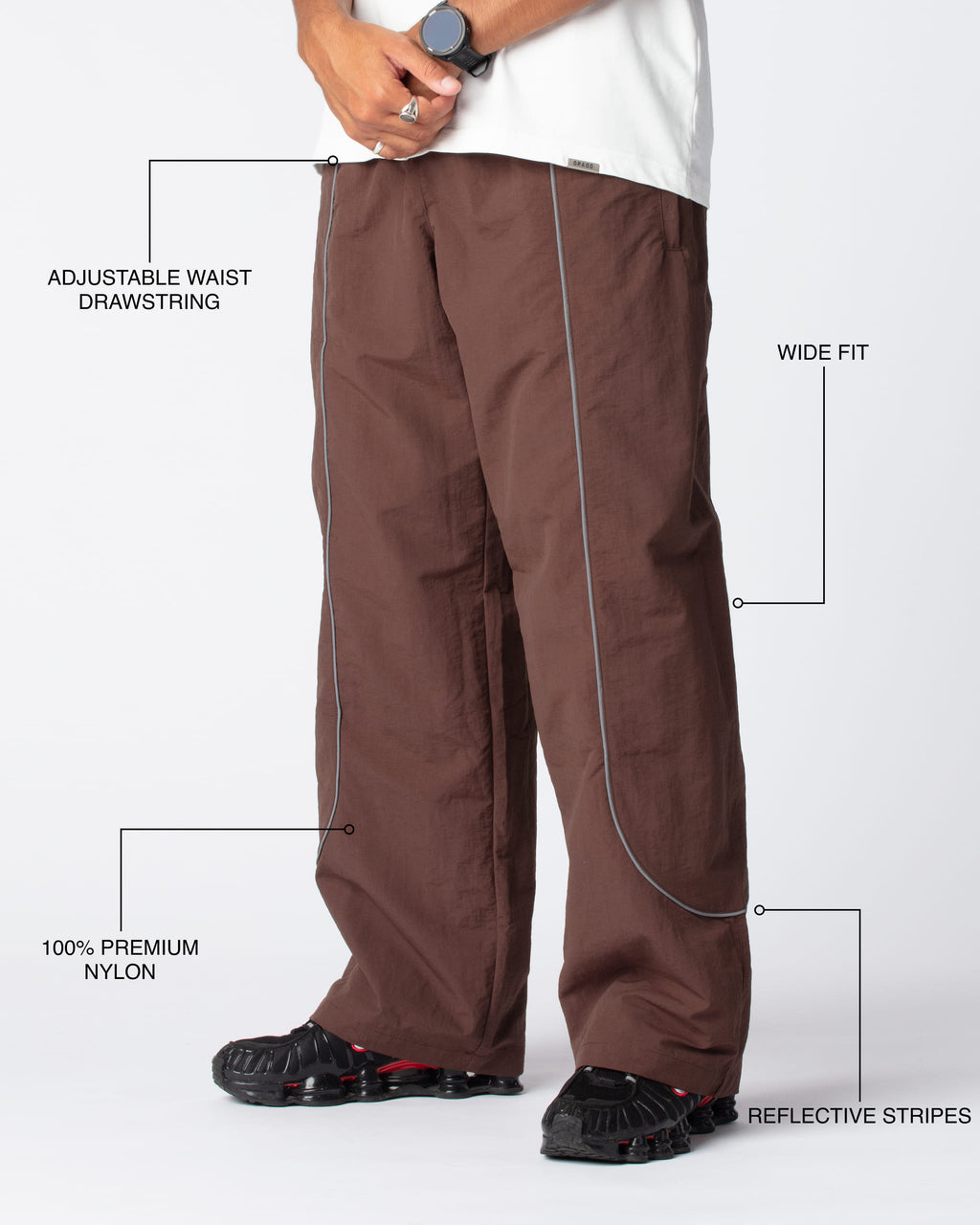 Diagonal Track Pants Cacao shot, showing adjustable waist drawstring, wide fit, premium nylon material and signature curved reflective stripes
