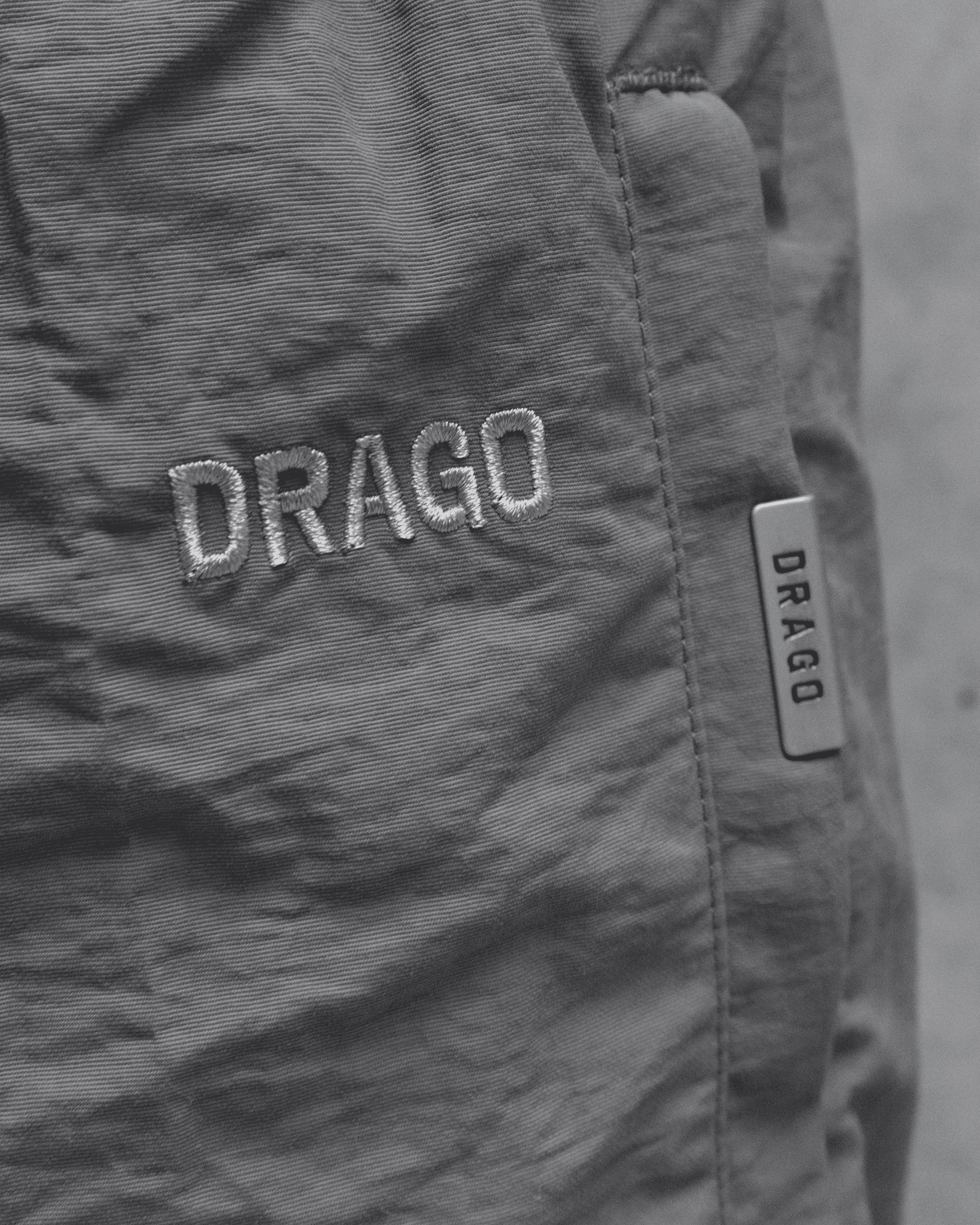 A close up shot of the tonal embroidered logo and signature metal band detail on our Track Pants Steel