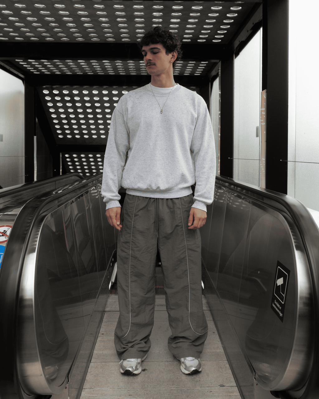 Marco standing in the entrance of an escalator in our Track Pants Steel