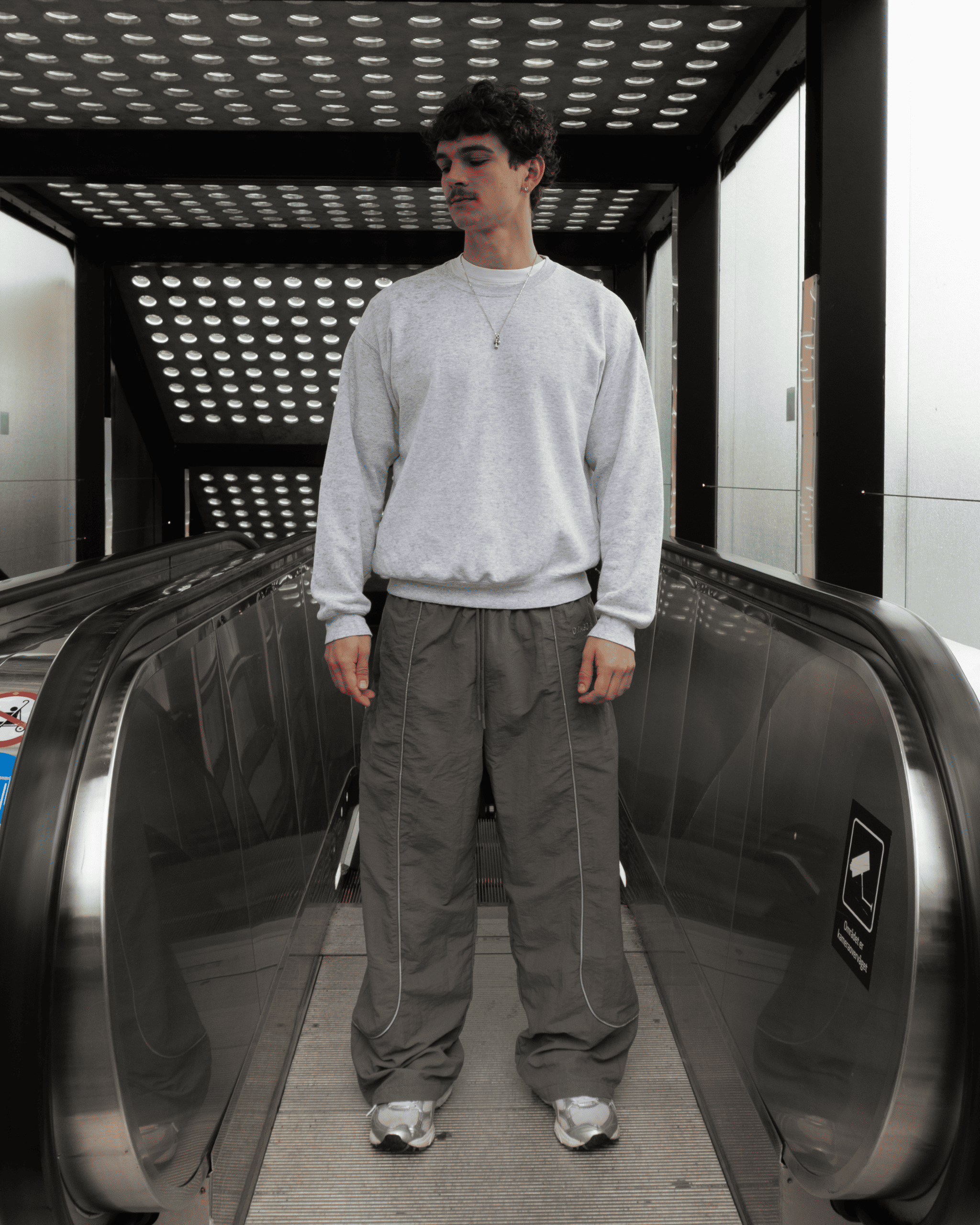 Marco standing in the entrance of an escalator in our Track Pants Steel